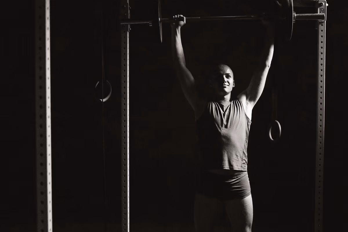 A coach watching a lifter press overhead in a dark room