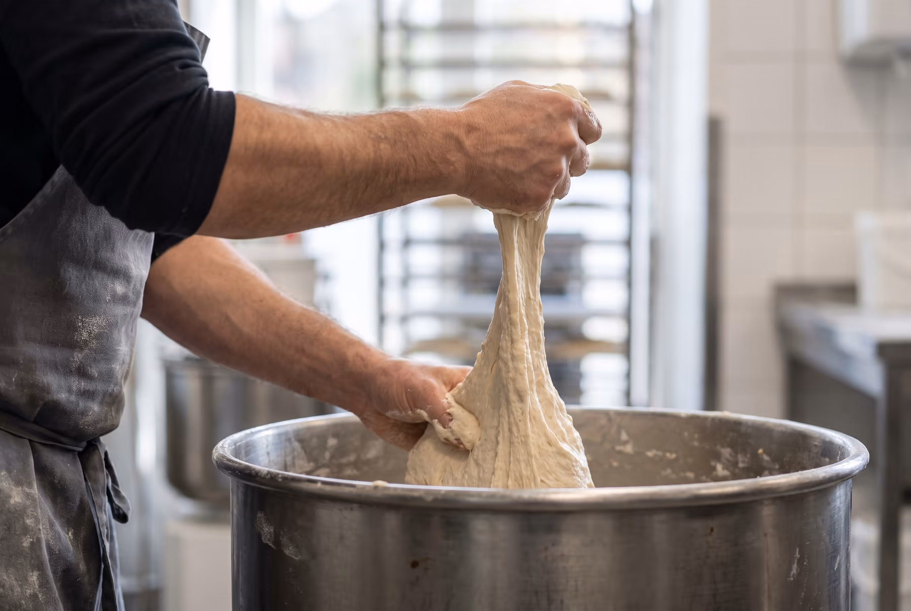 A baker lifting a batch of dough out of the mixing bowl