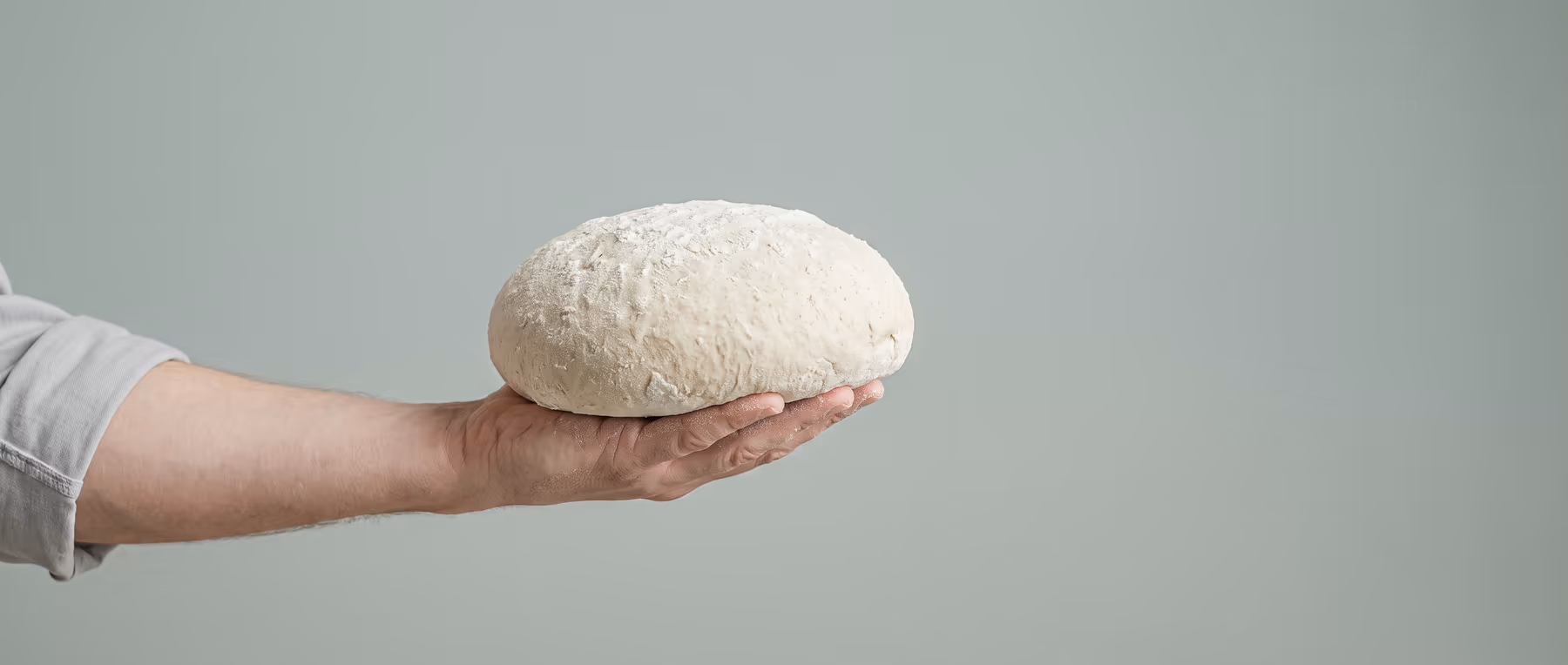 A hand holding a single round of proved dough