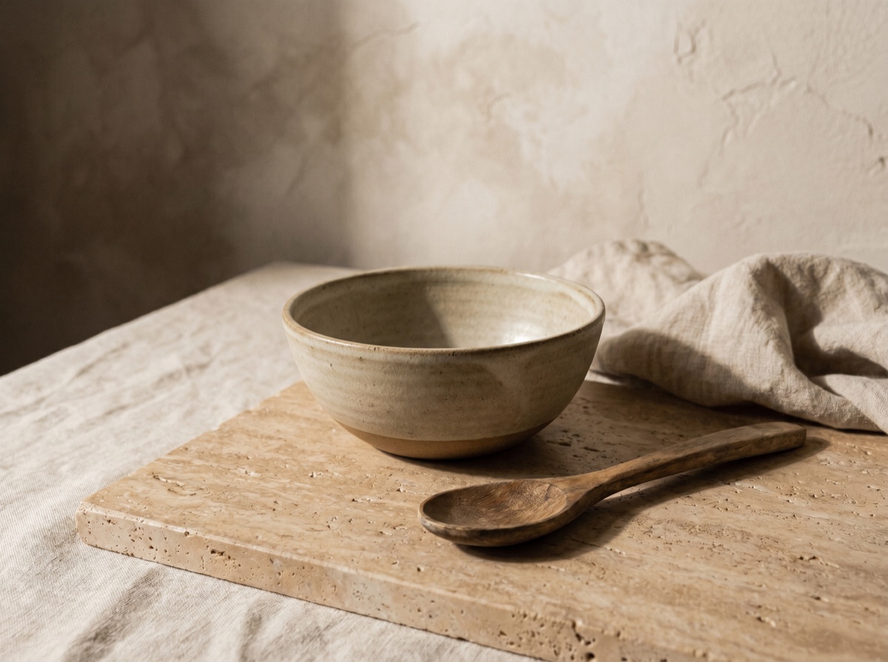 A stoneware bowl and spoon on warm stone, deep shadow