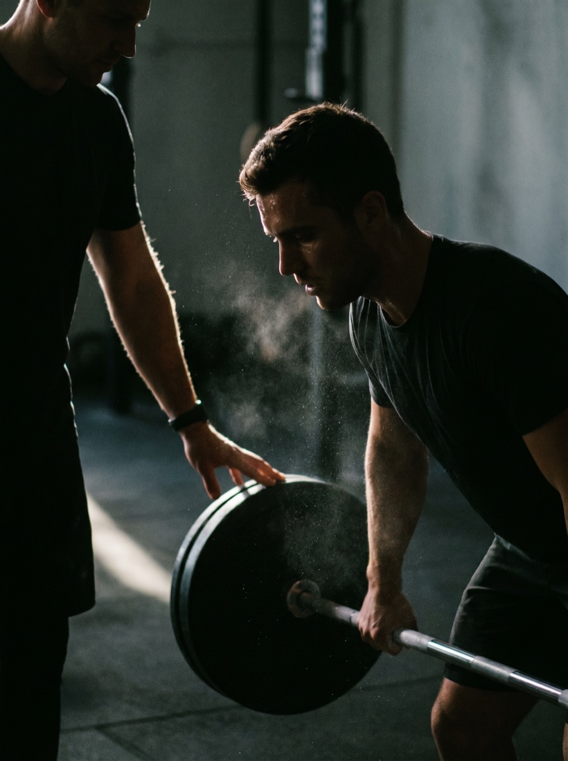 A coach cueing a single athlete through a lift in a quiet studio — focused, one-on-one, soft directional light