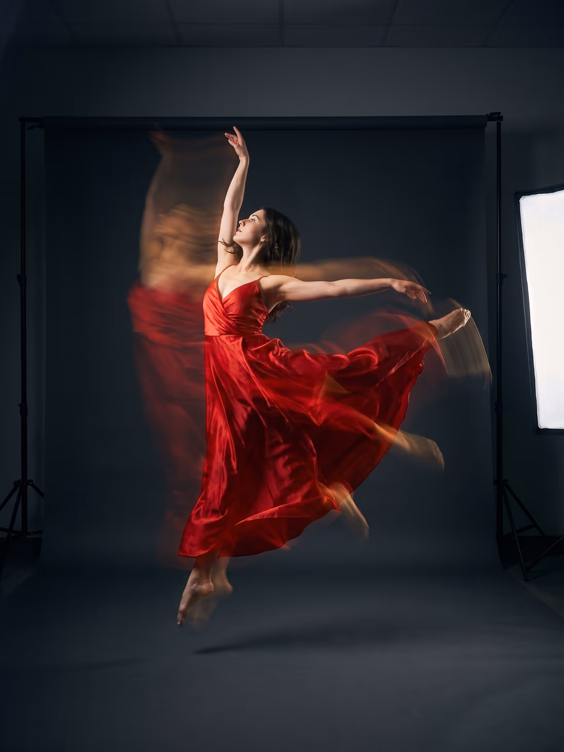 A dancer mid-leap in scarlet silk against a charcoal seamless backdrop