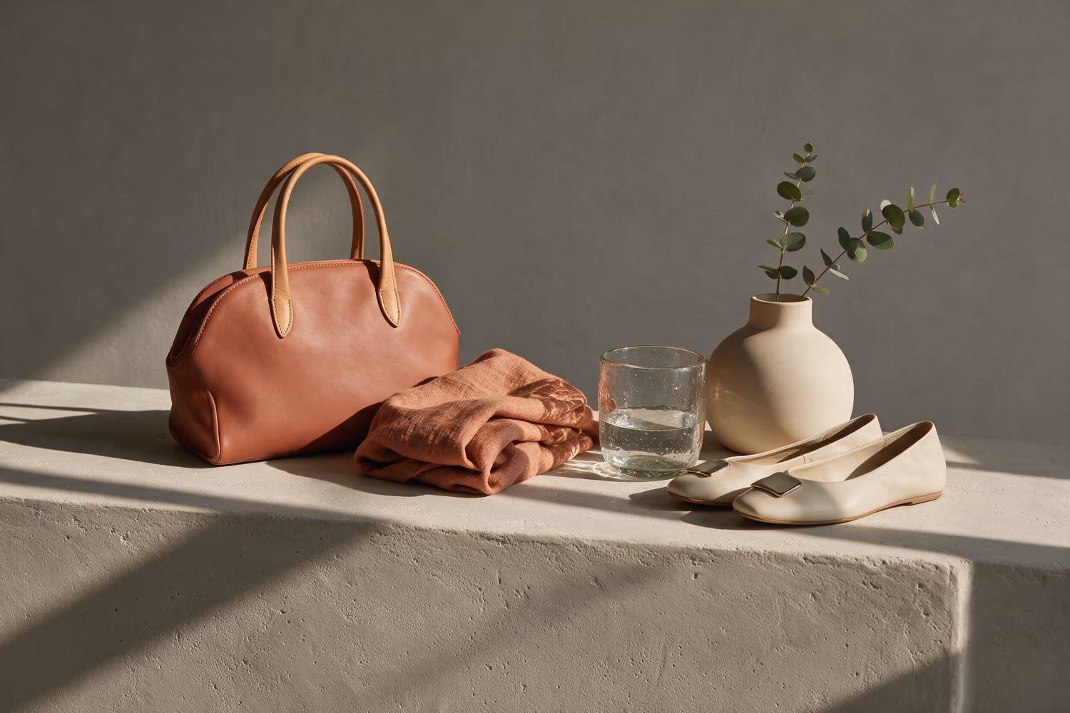 Leather accessories and glass objects on a plaster plinth under raking light