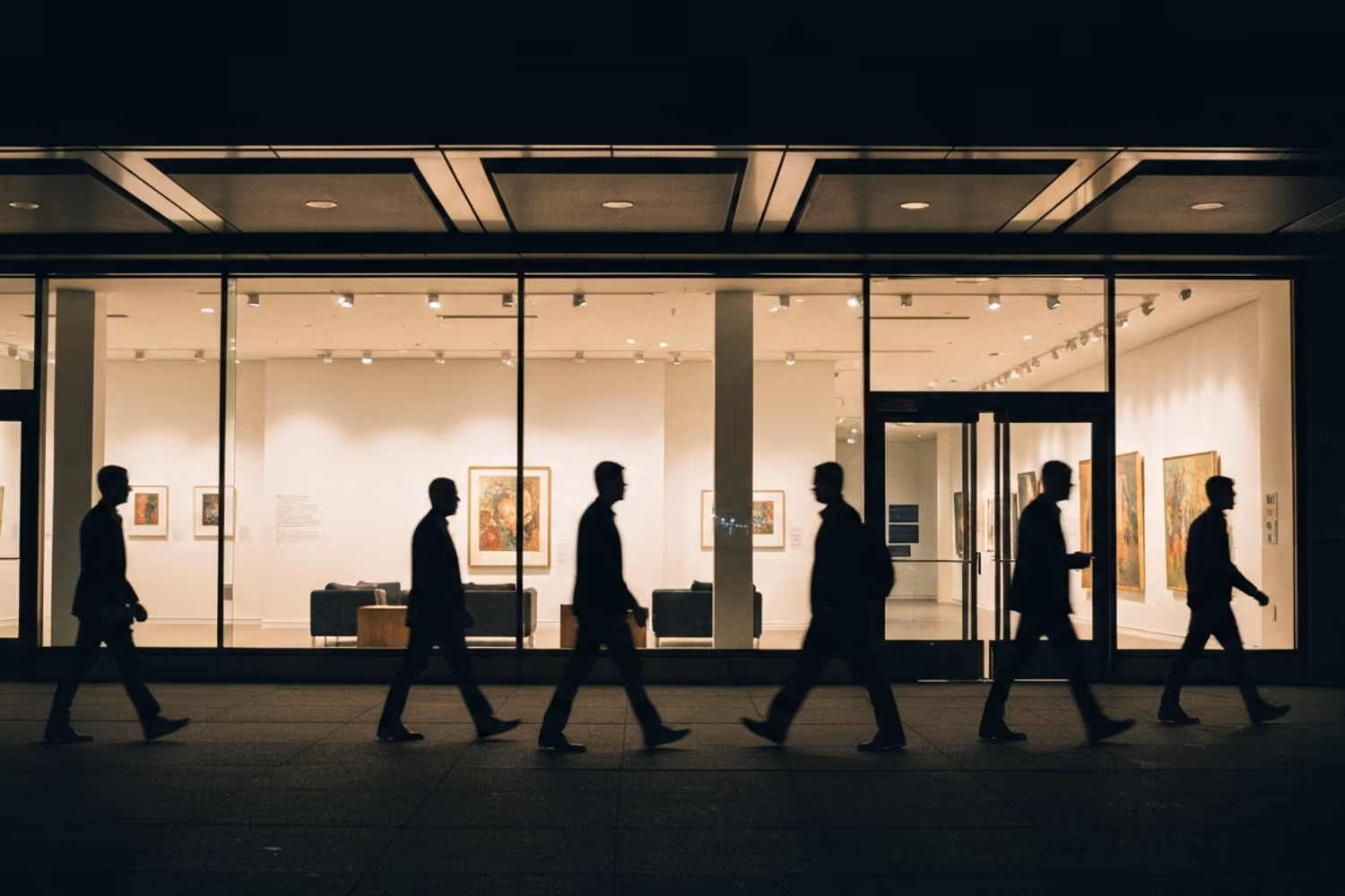 Silhouettes passing a lit gallery window at night